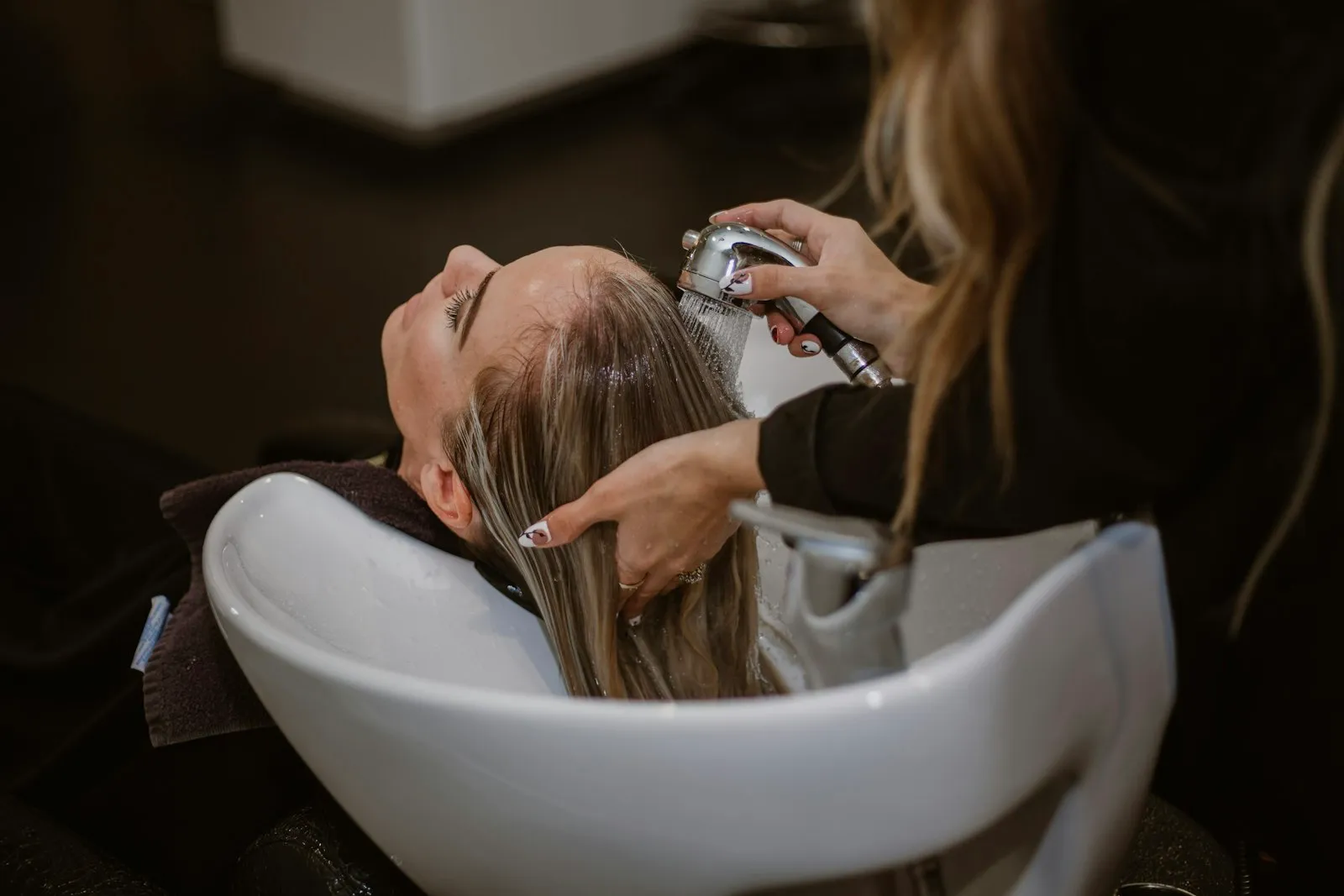 Fryzjerka myjąca włosy klientce przy stanowisku w salonie fryzjerskim