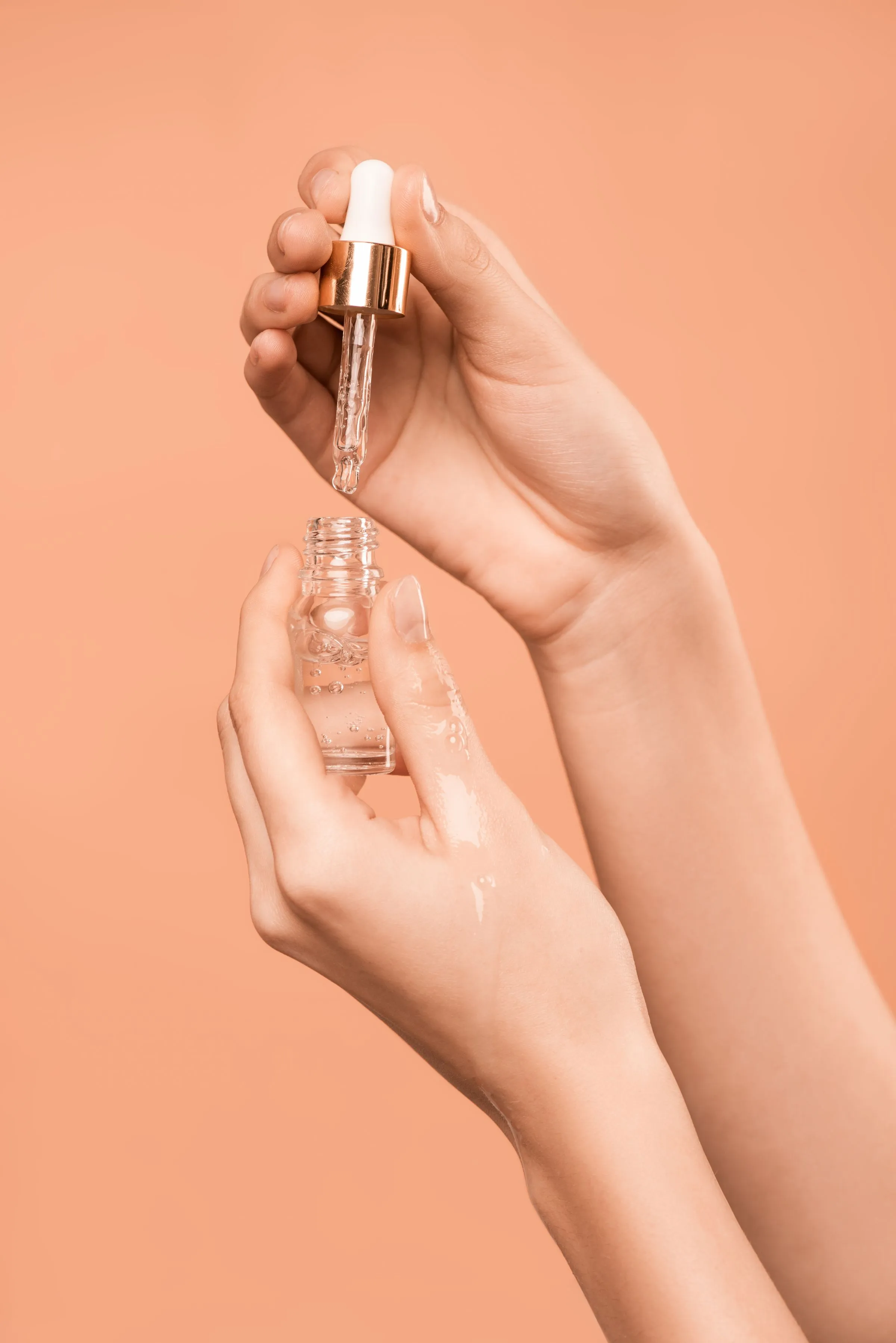 Dłonie z pipetą i flakonikiem serum pielęgnacyjnego na ciepłym tle